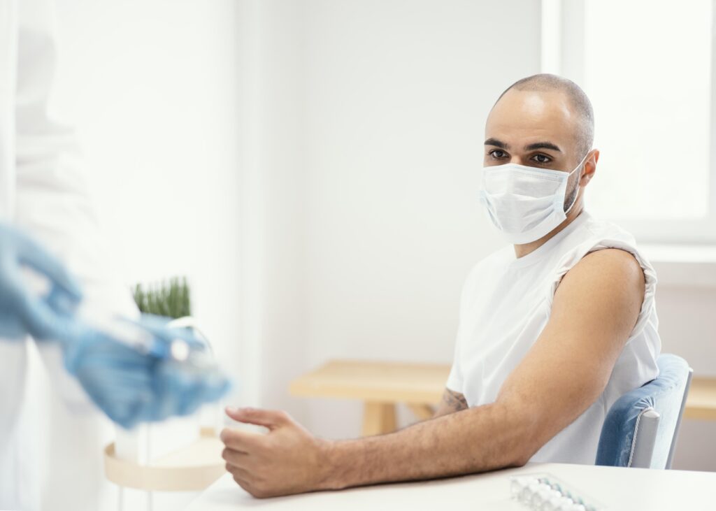 A young man in a white t-shirt with the sleeve rolled up waits for a vaccine to be administered.