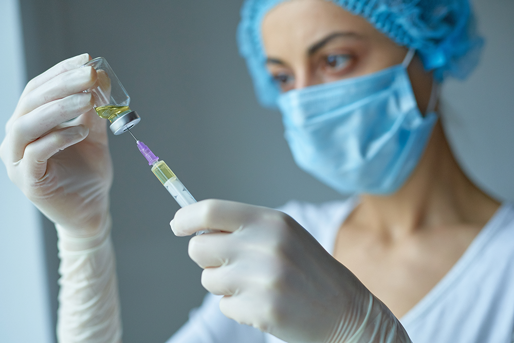 Female healthcare practitioner inserts a syringe into a small vial containing influenza vaccination medicine.